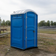 Baño químico portátil colocado en un entorno de obra al aire libre, vista lateral, sin personas.
